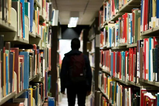 Student walking down a row of books in a library.